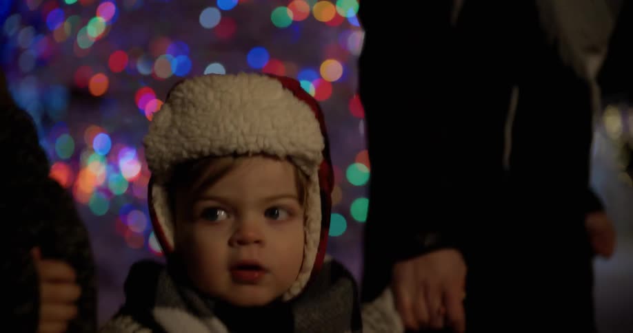 Child holding hands with adults walking outside at night near colored lights