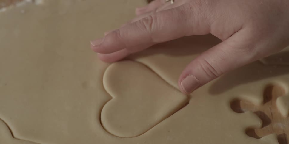 A woman cuts out a heart shaped sugar cookie