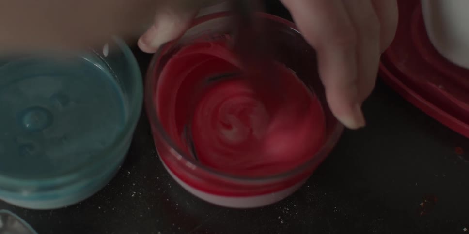 Food coloring is mixed into a bowl of frosting
