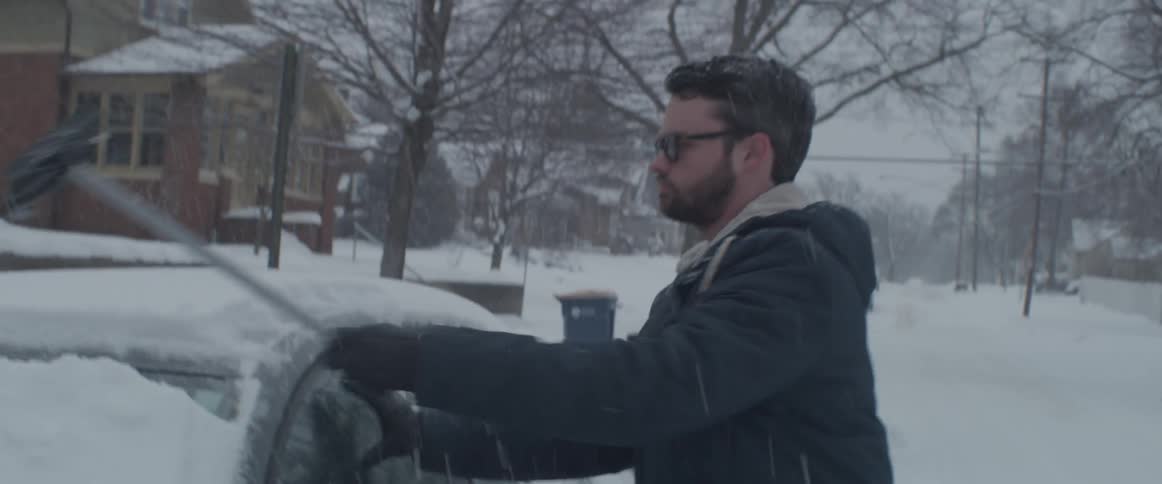 Man scrapes snow off his car windshield