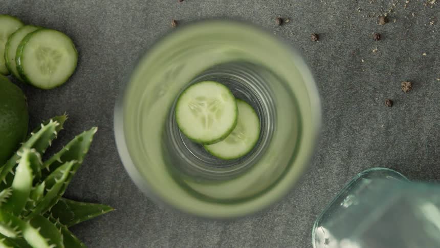 Cucumber slices are dropped into a glass tumbler