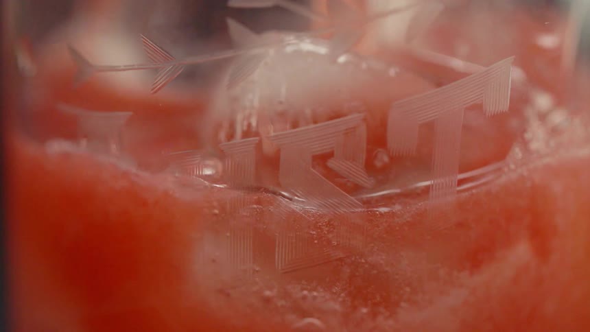 A pink drink is poured into a glass of ice