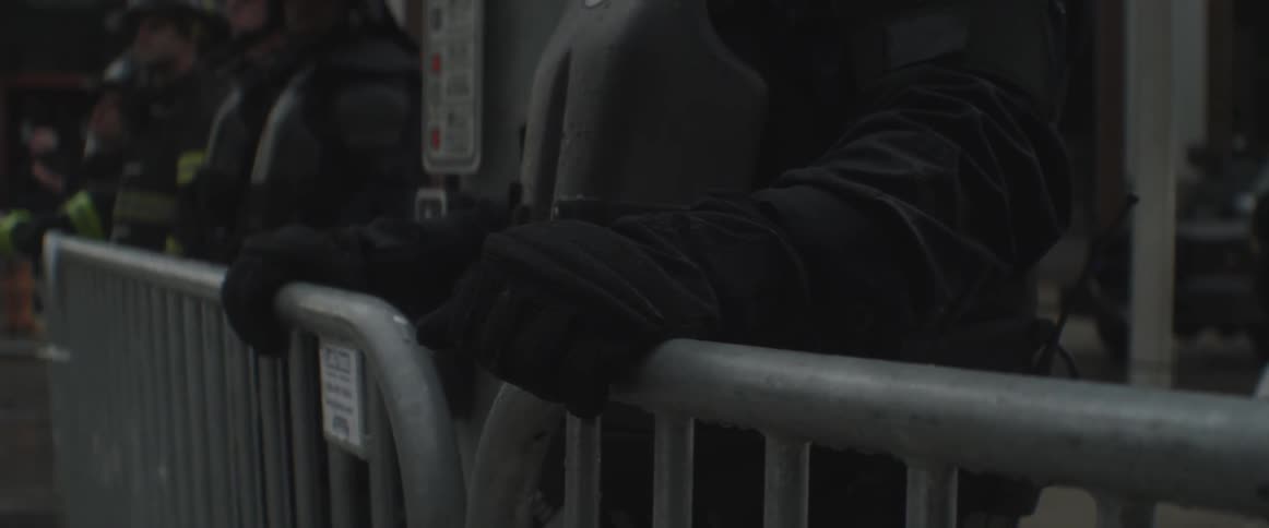 Closeup on the gloved hands of a cop standing behind a barricade