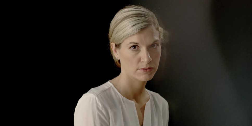 A woman in a white shirt is looking at the camera