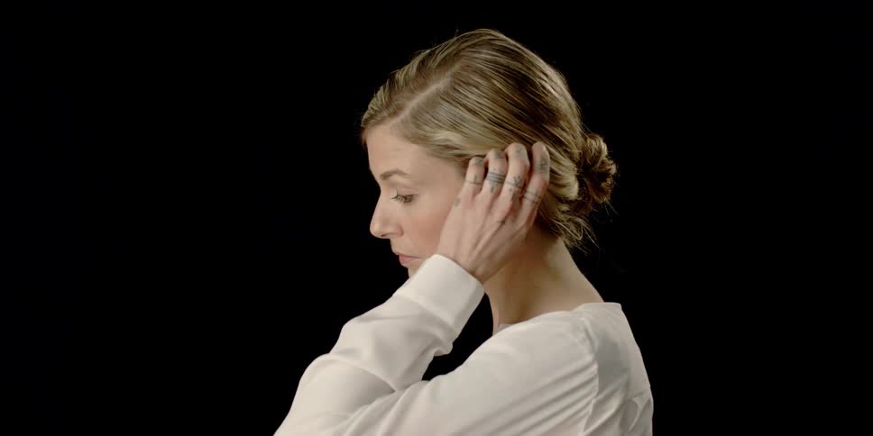 A woman touches her neck, adjusts her hair, and looks away