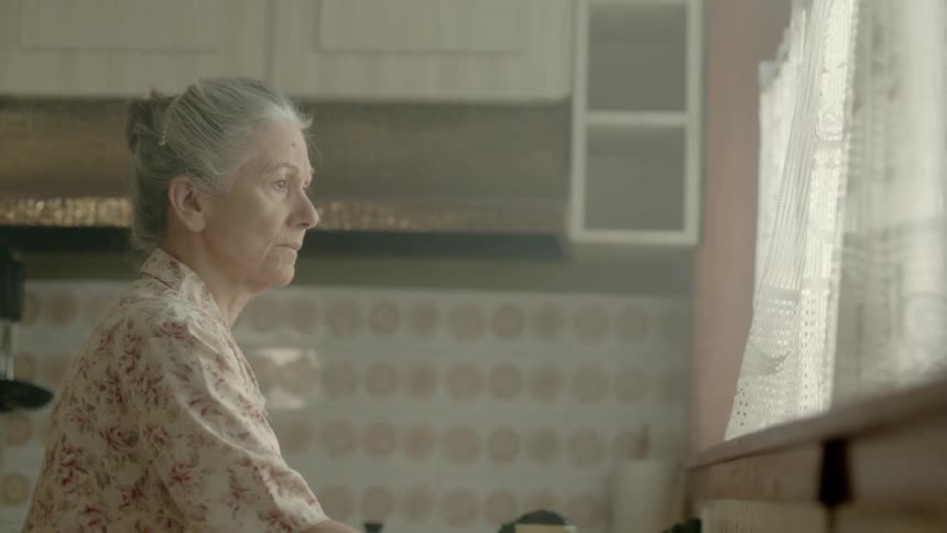 An older woman is cleaning out her tea pot and she's looking out the window