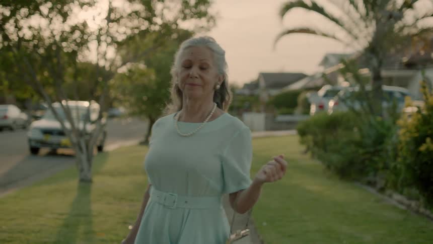 An older woman is dancing as she walks down the street