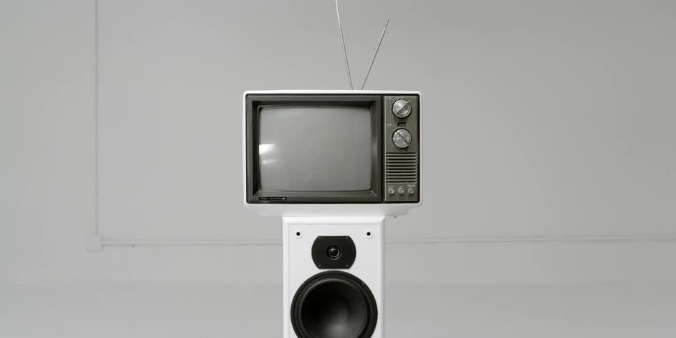 An old tv sits on top of a tall set of speakers