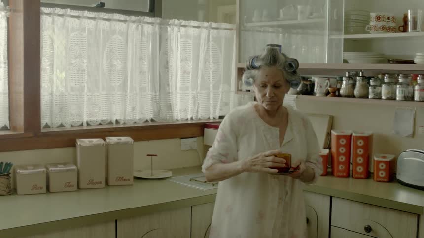 An older woman is getting cups down from the cabinet for tea and she replaces one of them