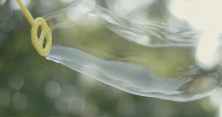 Bubbles are blown from a wand outdoors during the day