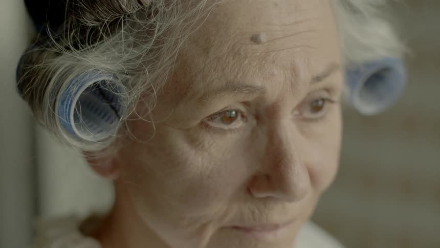An old woman with curlers in her hair stares ahead