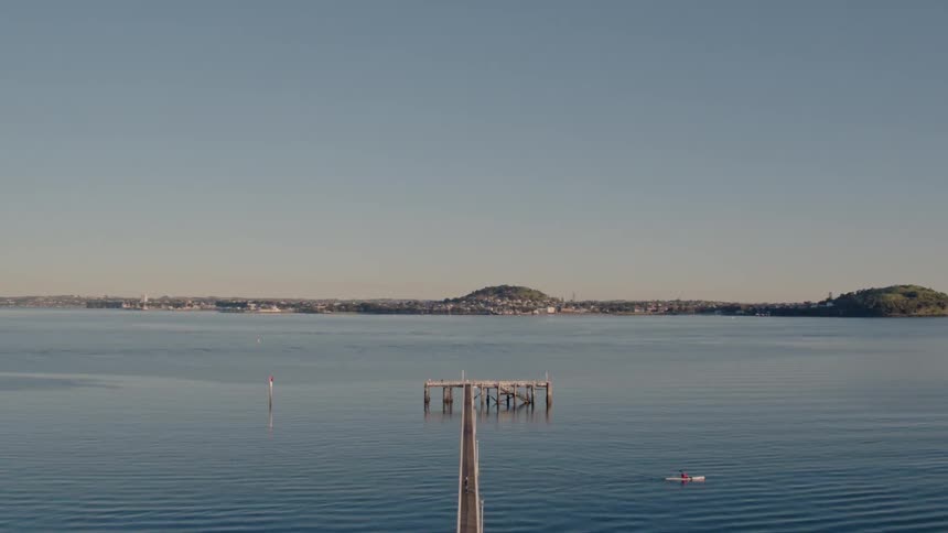 A kayaker passes beneath a pier on a sunny day