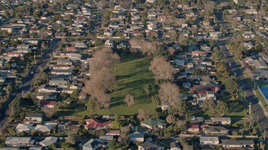 A small neighborhood with a park in the middle of being filmed from the air