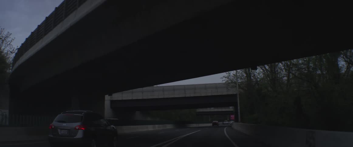 Vehicles moving down a road with a few overpasses above