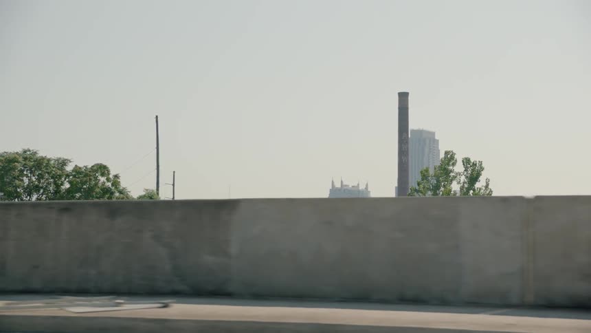 Smokestacks and skyscrapers are visible from the roadway