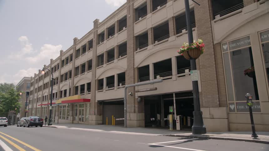 A parking garage is being filmed from the street as cars pass by