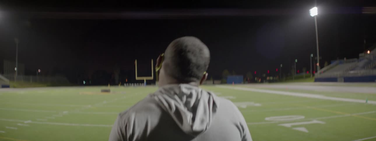 A man walks out onto a football field in an empty stadium at night