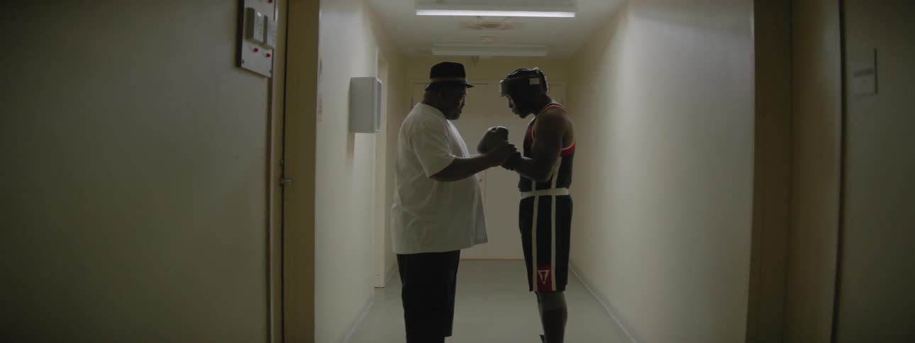 A boxer and coach talk in a hallway