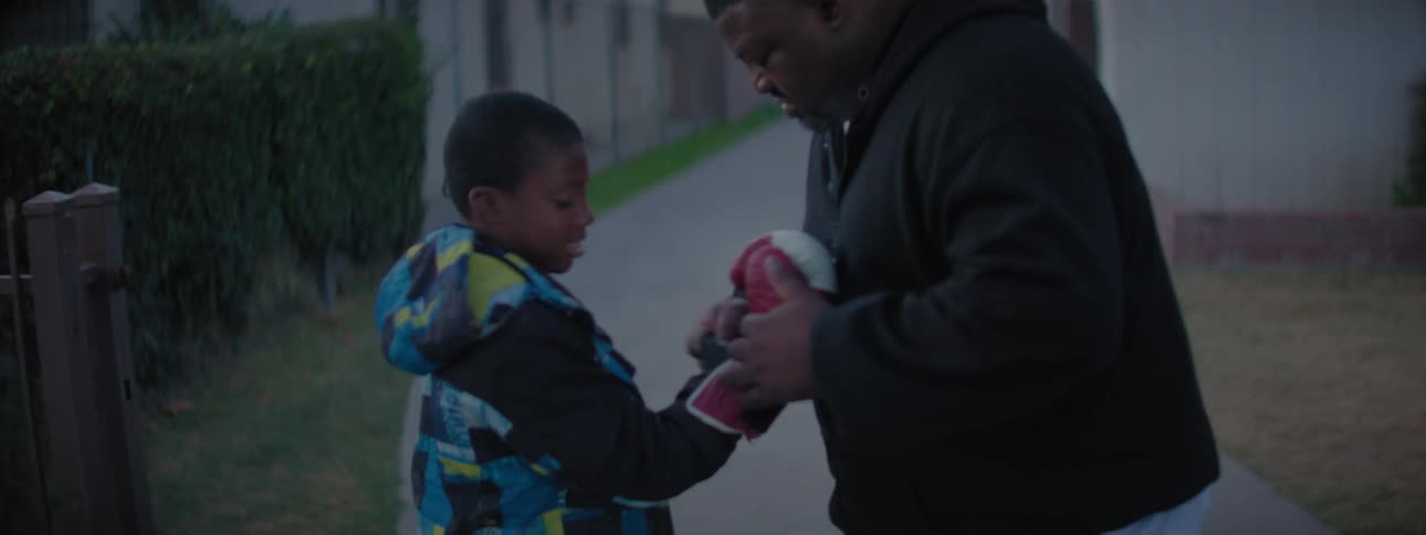 Man helps a boy put small boxing gloves on outside