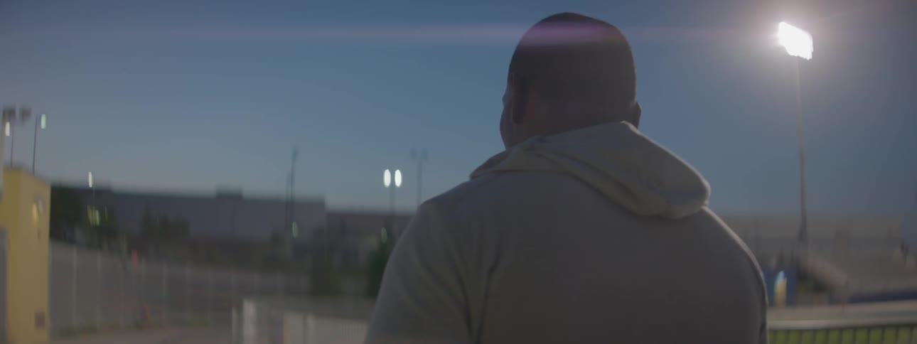 Man wearing a hoodie walking around a track at dusk in a city