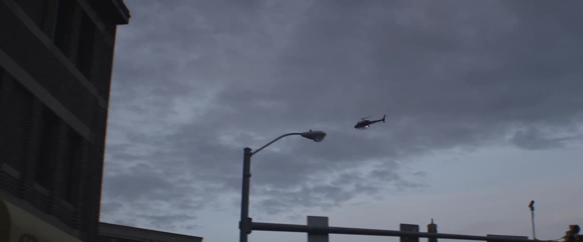 A helicopter flies over buildings at dusk