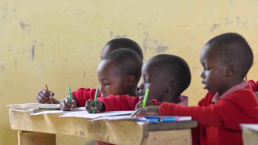 School kids sit at desks with crayons and paper