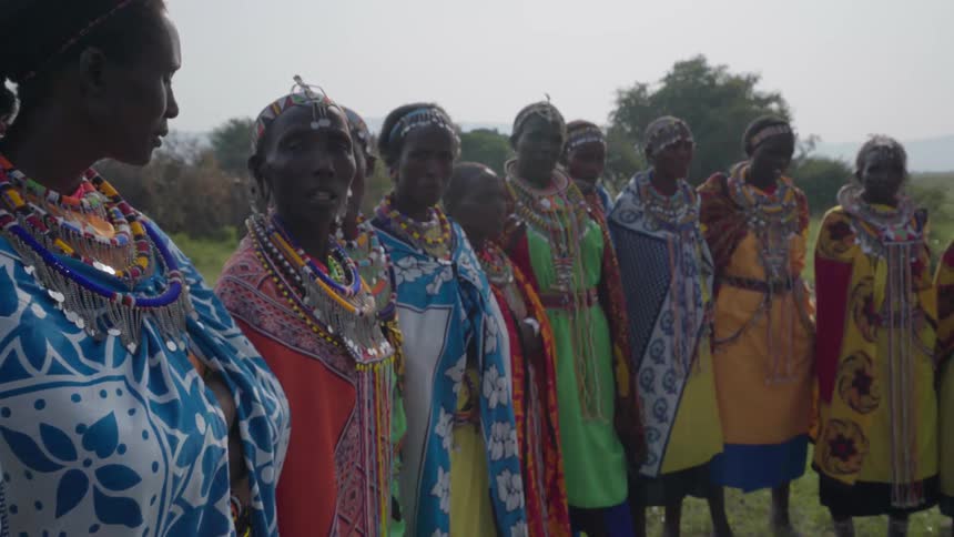 Maasai women in native dress and jewelry stand outside in a line
