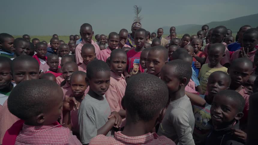 Crowd of villagers stand outside in the middle of a field