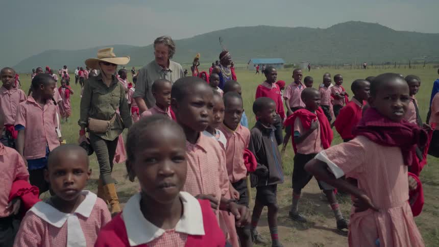 A couple of people are walking with a large amount of african school children