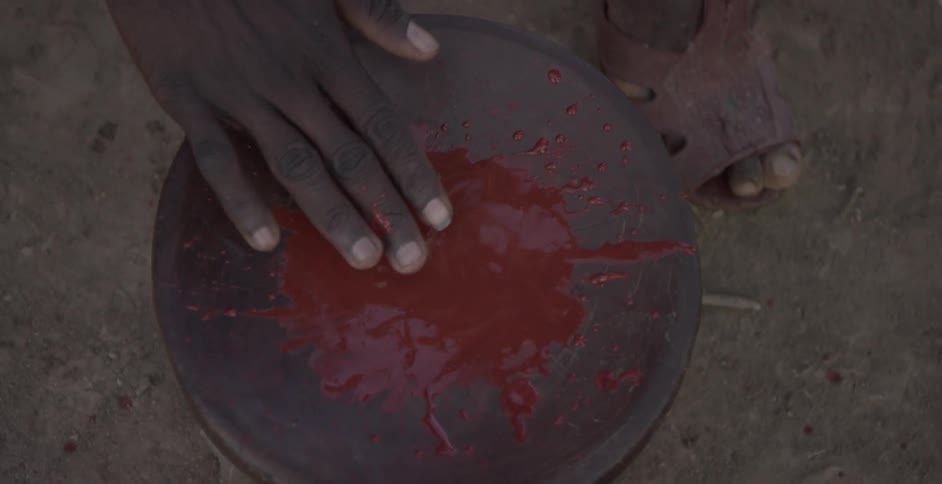 Maasai mixes red paint on a drum