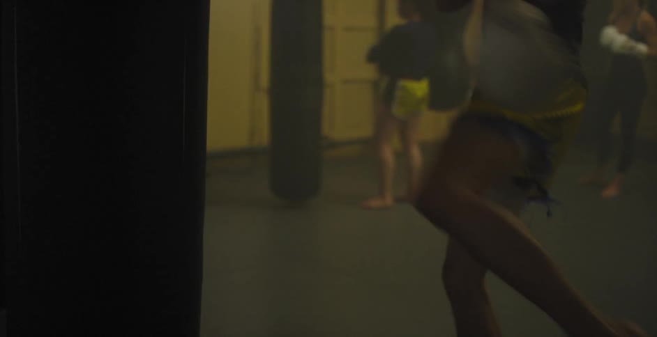 Fighter wearing boxing gloves is kicking a heavy bag while working out in a gym