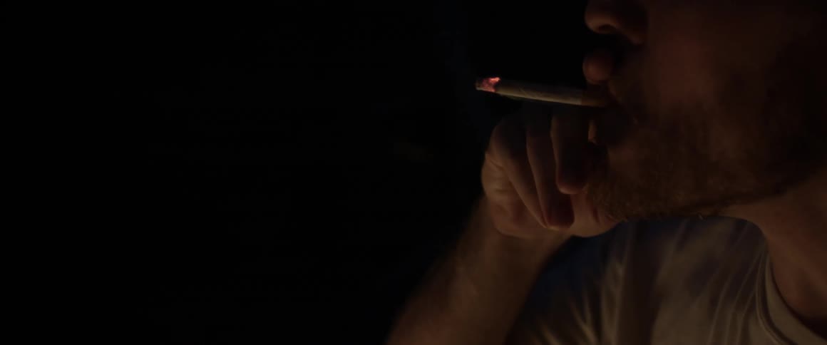 A man is smoking a cigarette outside at night