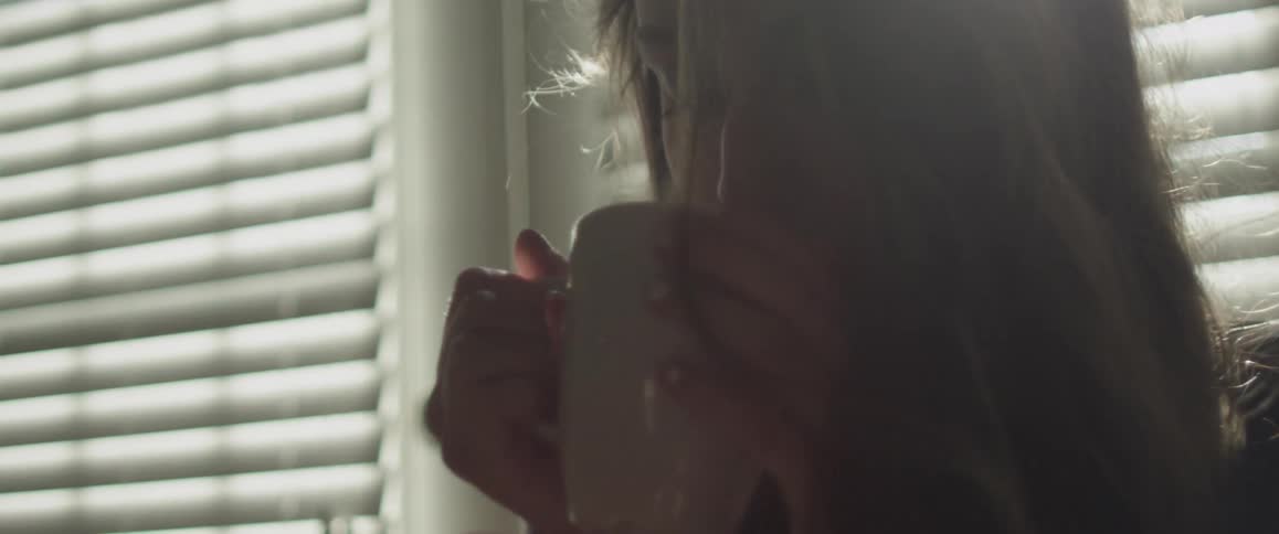 Woman sips from a mug as sunlight streams through the window