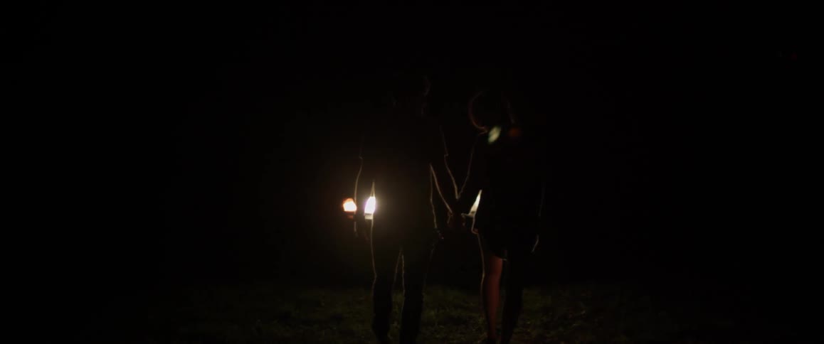 A man and woman hold hands outside at night