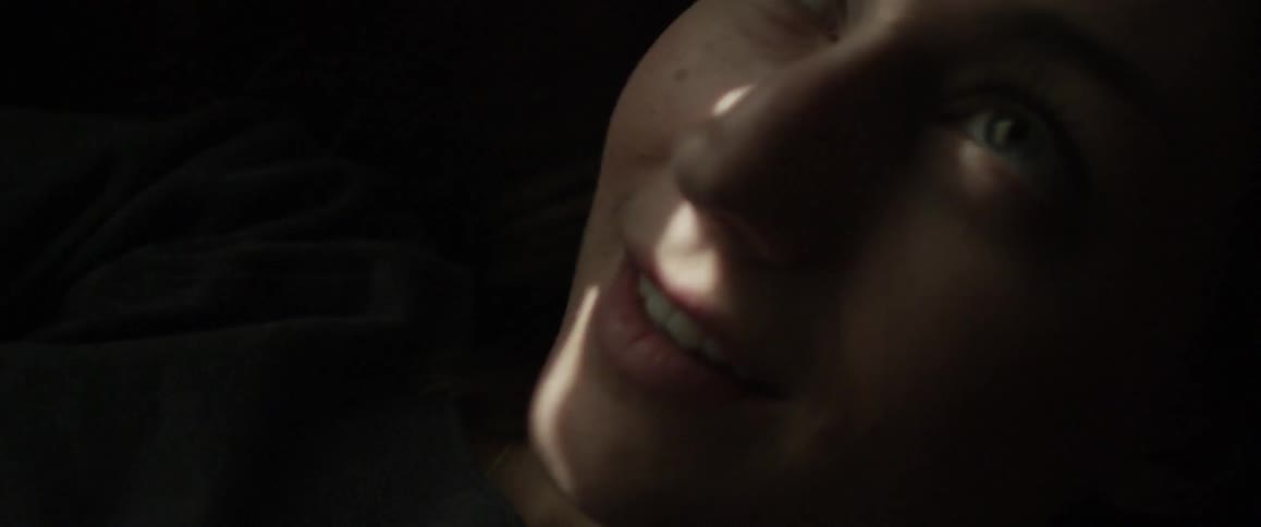 Woman smiling while looking upward as bits of light shine on her face