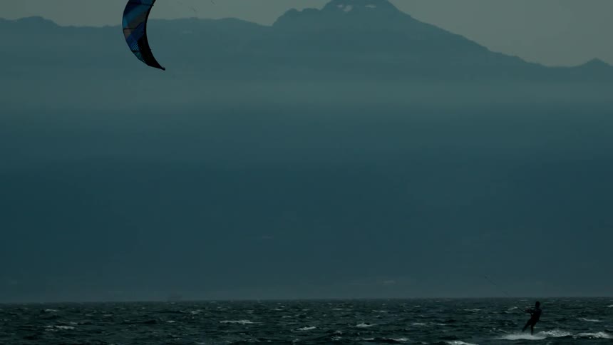 A kiteboarder is pulled across the ocean on a hazy day