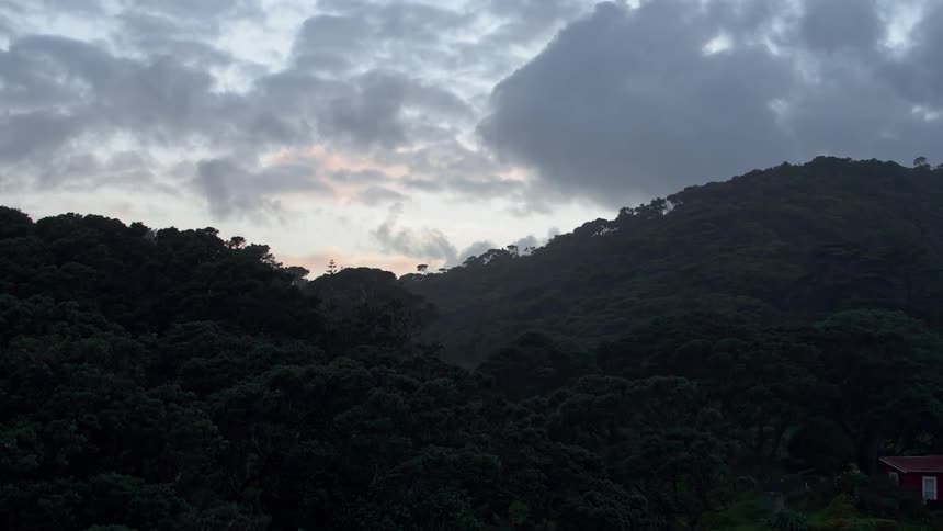 Clouds hang above a tree covered mountain