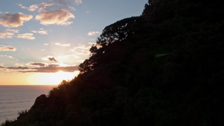 The sun is setting beyond cliffs on the coast