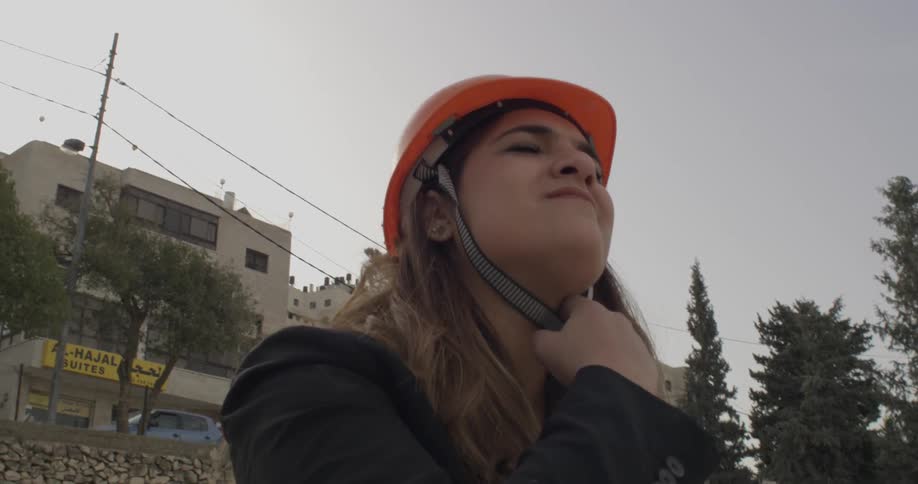 A woman puts on a hard hat as she stands at a construction site