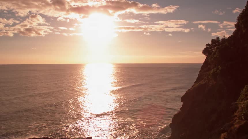 The sun is setting beyond cliffs on the coast