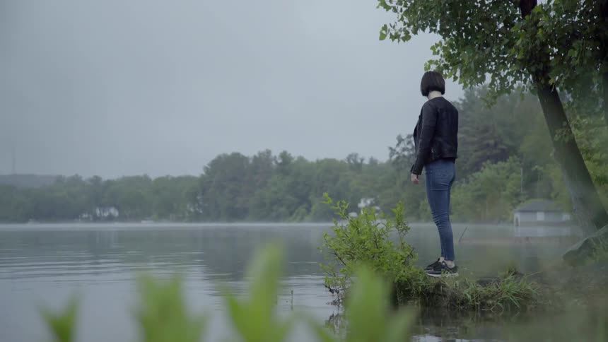 A woman stands on a rock on the shore of a lake on a misty day