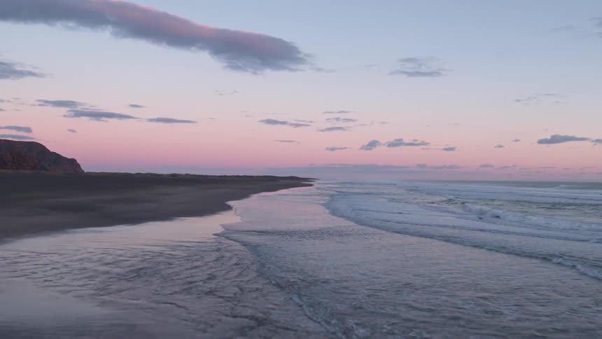 Birds fly low over waves lapping a beach at dusk