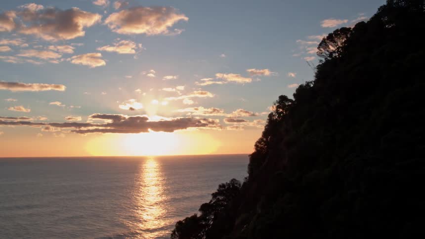The sun is setting at a beach beyond mountain cliffs