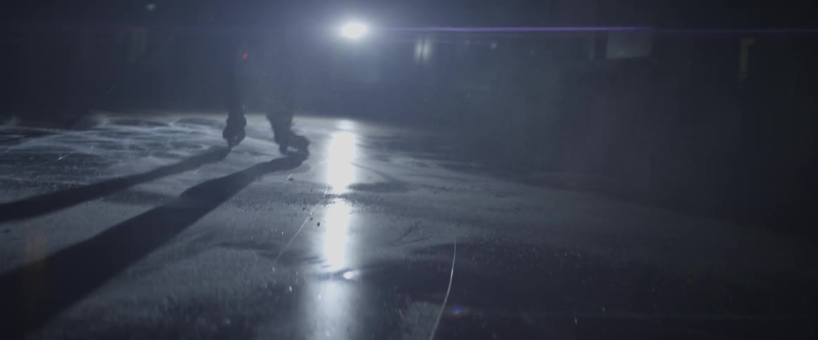 A hockey player is skating back and forth on a rink at night