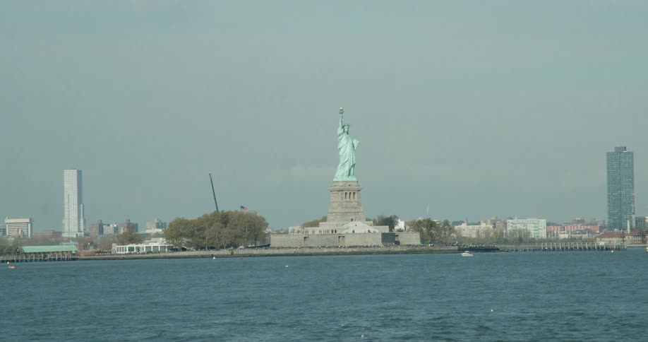 Boats travel past the statue of liberty on a sunny day