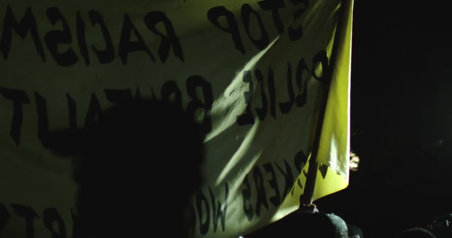 A sign is held in protest at night