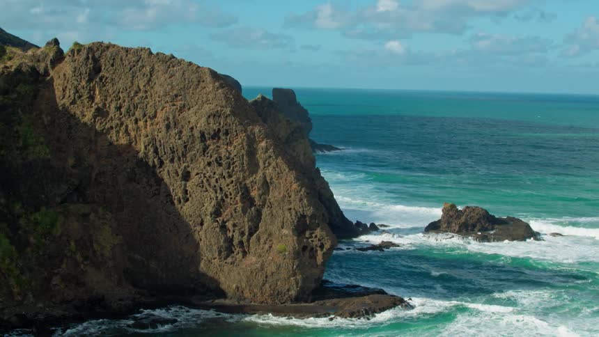 Waves crash over rocks and at the base of cliffs