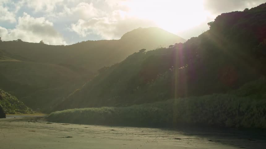 The sun casts rays over a mountain range and valley