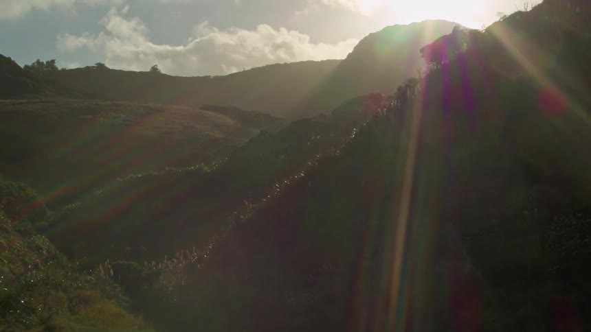 The sun beams down on island hills and a beach during the day