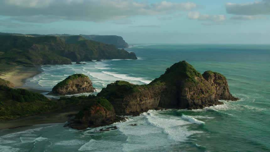 Waves crash over rocks at the base of cliffs as they roll toward the beach